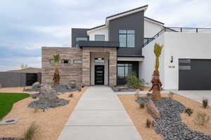 Modern home with driveway, stone siding, stucco siding, a balcony, and a garage