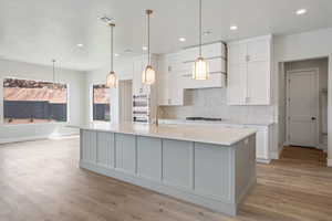 Kitchen featuring white cabinets, gas cooktop, multiple ovens, and light countertops
