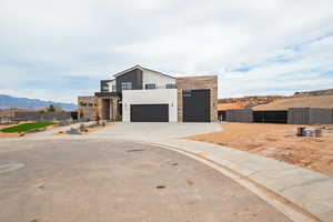 Contemporary home with stone siding, fence, concrete driveway, stucco siding, and a mountain view