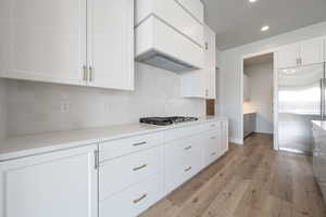 Kitchen featuring light wood finished floors, premium range hood, gas stovetop, built in refrigerator, and white cabinets