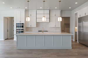 Kitchen featuring an island with sink, light countertops, white cabinetry, stainless steel appliances, and decorative backsplash