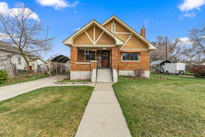 View of front of house featuring a chimney, a front yard, brick siding, a carport, and concrete driveway