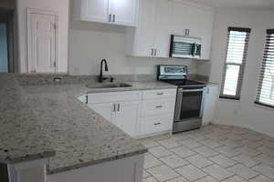 Kitchen featuring light stone counters, a sink, white cabinetry, a peninsula, and stainless steel appliances