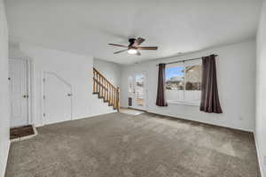 Unfurnished living room featuring baseboards, stairs, ceiling fan, and carpet flooring