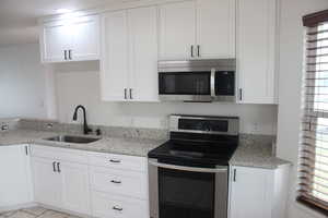 Kitchen featuring light stone counters, a sink, white cabinetry, light tile patterned floors, and stainless steel appliances