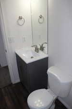Half bathroom with toilet, wood finished floors, and vanity