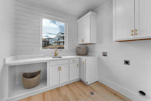 Laundry area featuring a sink, washer hookup, electric dryer hookup, light wood-style flooring, and cabinet space
