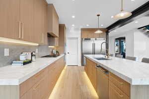 Kitchen with modern cabinets, light wood-type flooring, backsplash, and appliances with stainless steel finishes