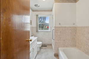 Bathroom with tile walls, toilet, a tub to relax in, an enclosed shower, and wainscoting