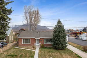 View of front facade featuring fence, a mountain view, a front lawn, brick siding, and a shingled roof