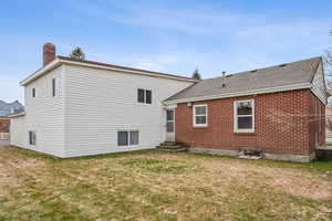 Back of house featuring a chimney, entry steps, a shingled roof, and a lawn