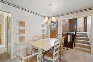 Dining room featuring baseboards, a chandelier, stairway, and light colored carpet