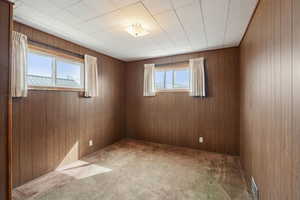 Carpeted spare room featuring visible vents and wood walls