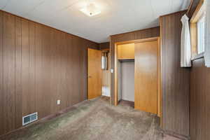 Unfurnished bedroom featuring a closet, carpet floors, visible vents, and wood walls