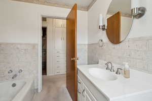 Full bath featuring vanity, a tub to relax in, tile walls, and wainscoting