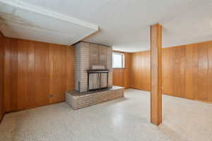 Unfurnished living room with a brick fireplace, wood walls, baseboards, and a textured ceiling