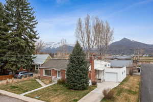 View of front of house with fence, brick siding, a front lawn, driveway, and a mountain view
