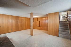 Finished below grade area featuring a textured ceiling, stairs, carpet flooring, and wooden walls