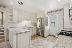 Kitchen with light countertops, a sink, a peninsula, and freestanding refrigerator