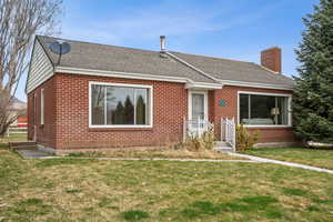 View of front facade featuring brick siding, a front yard, roof with shingles, and a chimney
