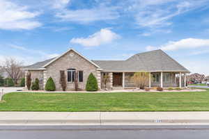 View of front facade featuring covered porch, brick siding, a front yard, and a shingled roof