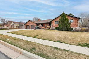 Ranch-style house with concrete driveway, an attached garage, a front yard, a porch, and a chimney