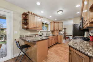 Kitchen featuring a kitchen breakfast bar, open shelves, dark stone countertops, a sink, and light wood finished floors