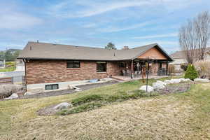 Rear view of property featuring fence, a chimney, brick siding, a lawn, and a patio area