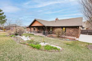 Back of property with a chimney, brick siding, roof with shingles, a lawn, and covered porch