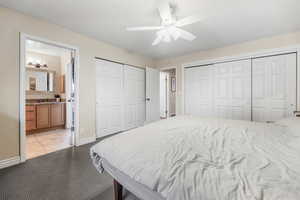 Bedroom with light colored carpet, baseboards, multiple closets, connected bathroom, and a ceiling fan