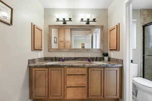 Full bathroom with toilet, a sink, double vanity, and a shower stall