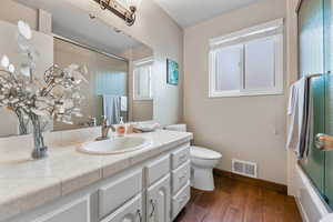 Full bath with vanity, toilet, baseboards, visible vents, and wood finished floors