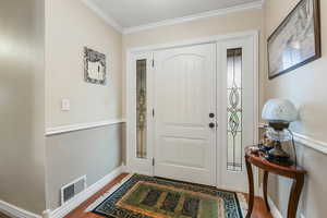 Foyer entrance featuring baseboards, visible vents, crown molding, and wood finished floors