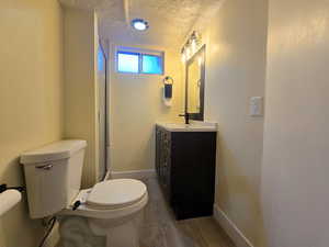 Full bath featuring toilet, a textured ceiling, vanity, wood finished floors, and a shower with door