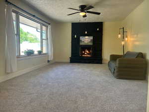 Living area featuring a ceiling fan, a textured ceiling, a large fireplace, and carpet