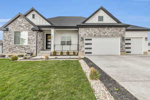 View of front of house with driveway, stone siding, an attached garage, board and batten siding, and a front lawn