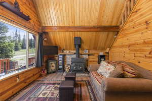 Living area featuring lofted ceiling with beams, wood walls, hardwood / wood-style floors, a wood stove, and wood ceiling