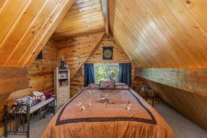 Bedroom featuring vaulted ceiling, wooden walls, wood ceiling, and carpet