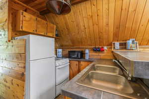 Kitchen featuring stainless steel countertops, wooden ceiling, a sink, wood walls, and white appliances