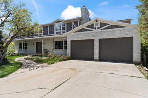View of front of property featuring a chimney, driveway, brick siding, covered porch, and an attached garage
