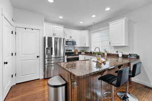Kitchen with a breakfast bar, a peninsula, dark wood-style floors, stainless steel appliances, and white cabinets