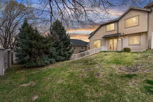Rear view of house featuring a lawn, fence, and stucco siding