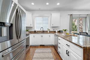 Kitchen with a peninsula, wood finished floors, stainless steel appliances, white cabinetry, and a sink