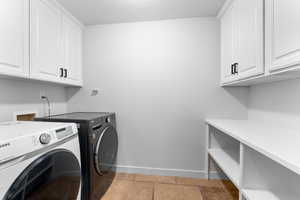 Laundry area with baseboards, separate washer and dryer, cabinet space, and stone tile flooring