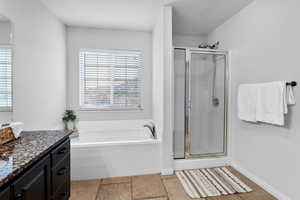 Bathroom featuring a bath, a stall shower, vanity, and stone tile flooring