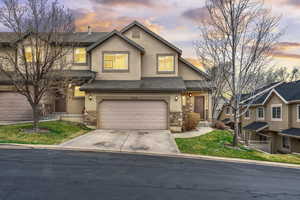 View of front facade featuring stone siding, a garage, driveway, and stucco siding