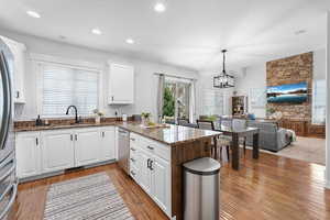 Kitchen with open floor plan, a chandelier, stainless steel dishwasher, light wood finished floors, and a peninsula