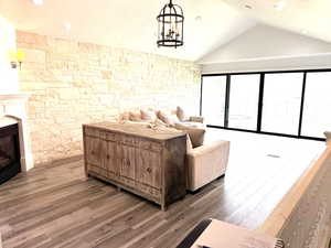Living area featuring vaulted ceiling, wood finished floors, a glass covered fireplace, and an inviting chandelier