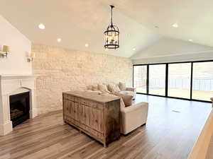 Living area with lofted ceiling, recessed lighting, light wood-style flooring, a notable chandelier, and a glass covered fireplace