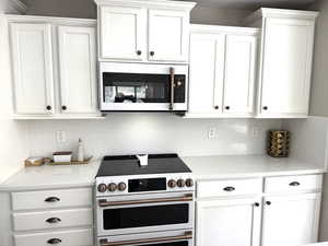 Kitchen featuring white cabinets, light quartz countertops, and white appliances